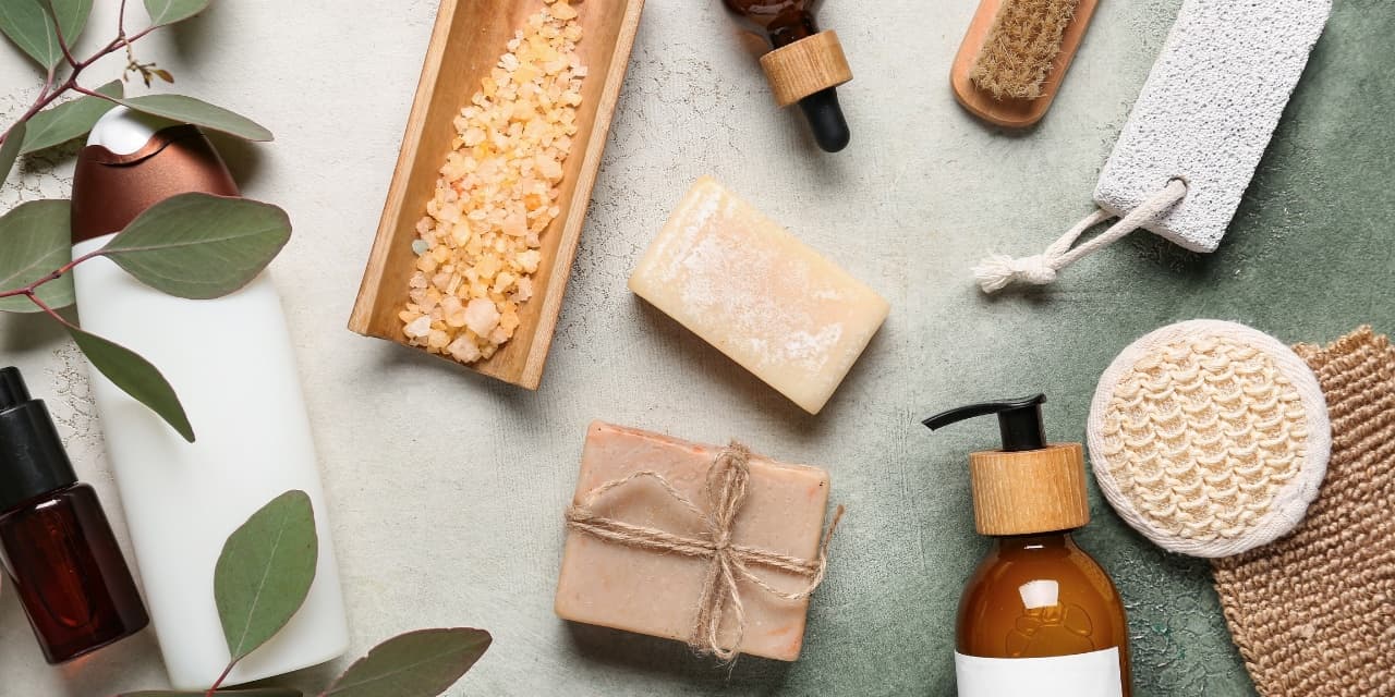 Flat lay of unlabeled beauty and wellness products — soap bars, salt scrub, dropper bottle, and eucalyptus